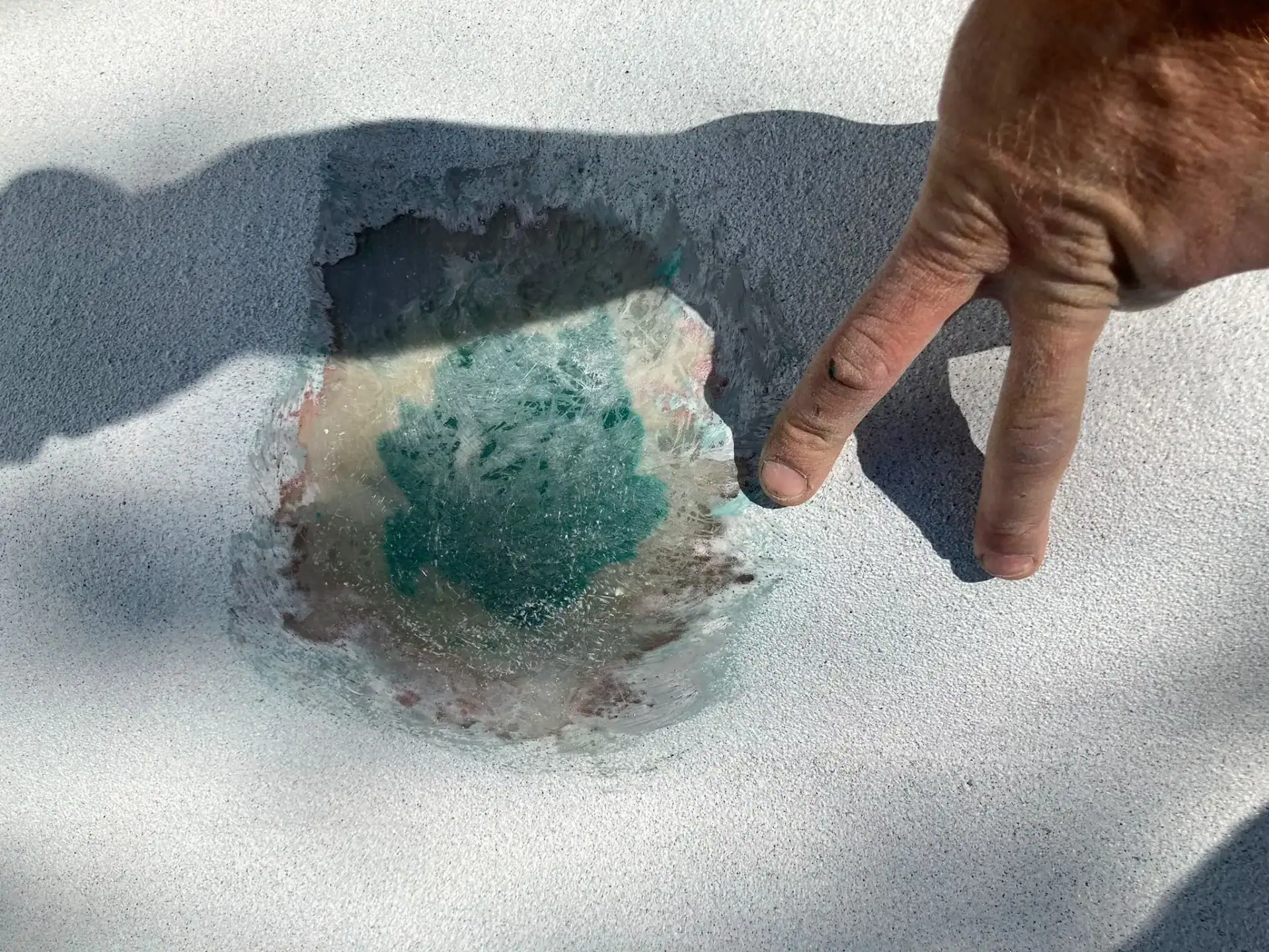 Main pointant un trou dans le liner de piscine en PVC.