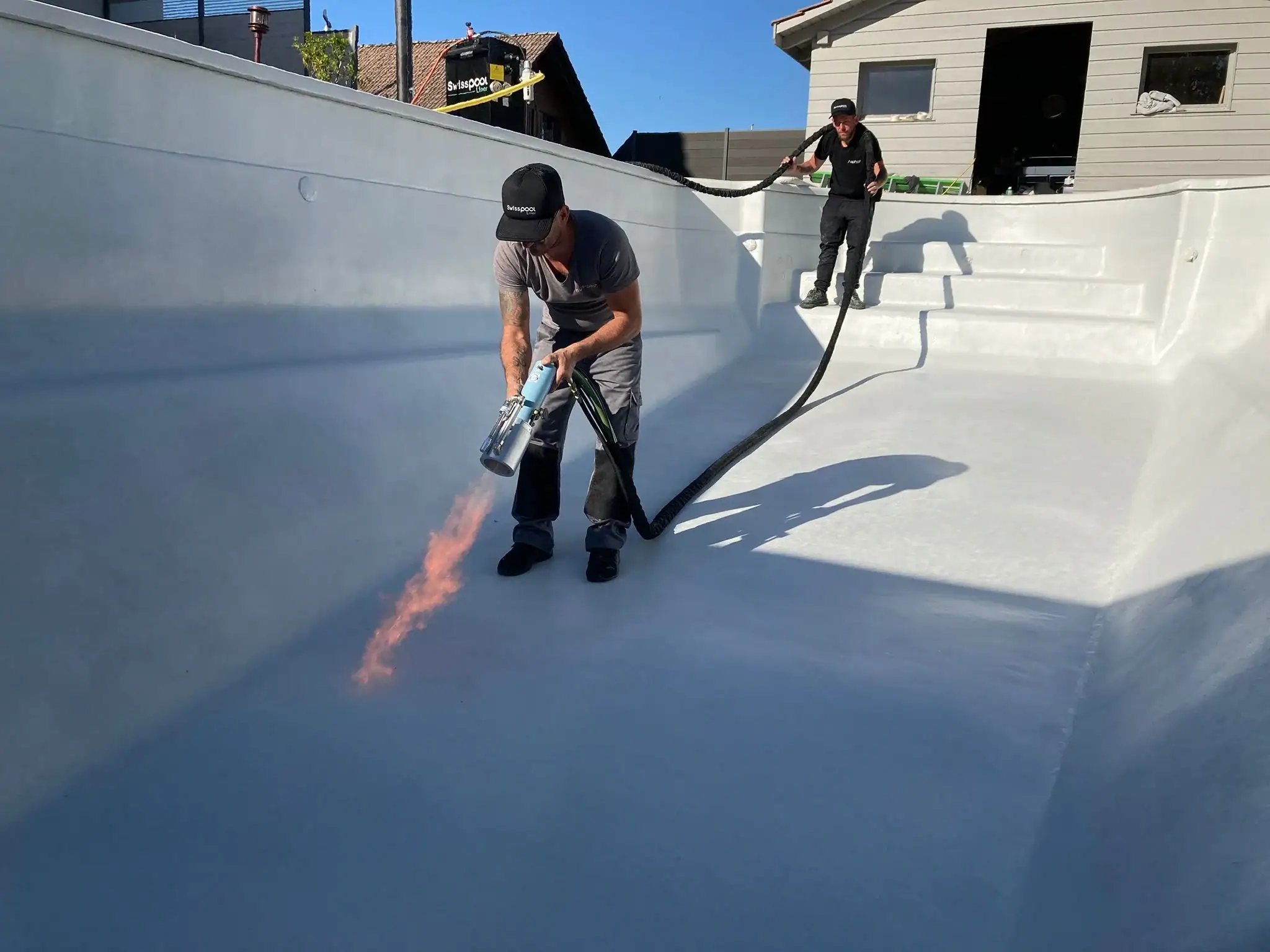Travailleurs appliquant un revêtement de protection dans une piscine vide.