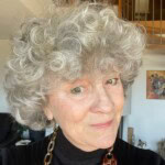 Vieux visage de femme aux cheveux gris bouclés et regard souriant en intérieur.