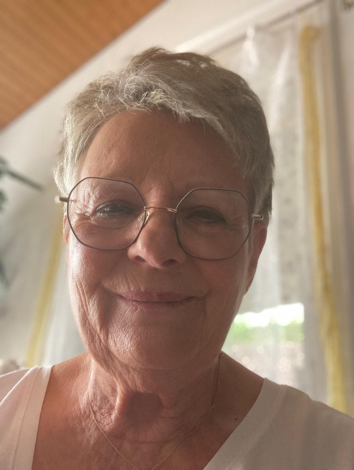 - Visage souriant d'une femme âgée portant des lunettes rondes.
